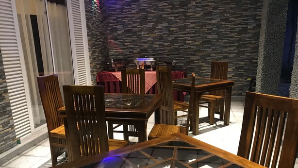 A dining area with wooden chairs and tables, a stone wall, and a red tablecloth.