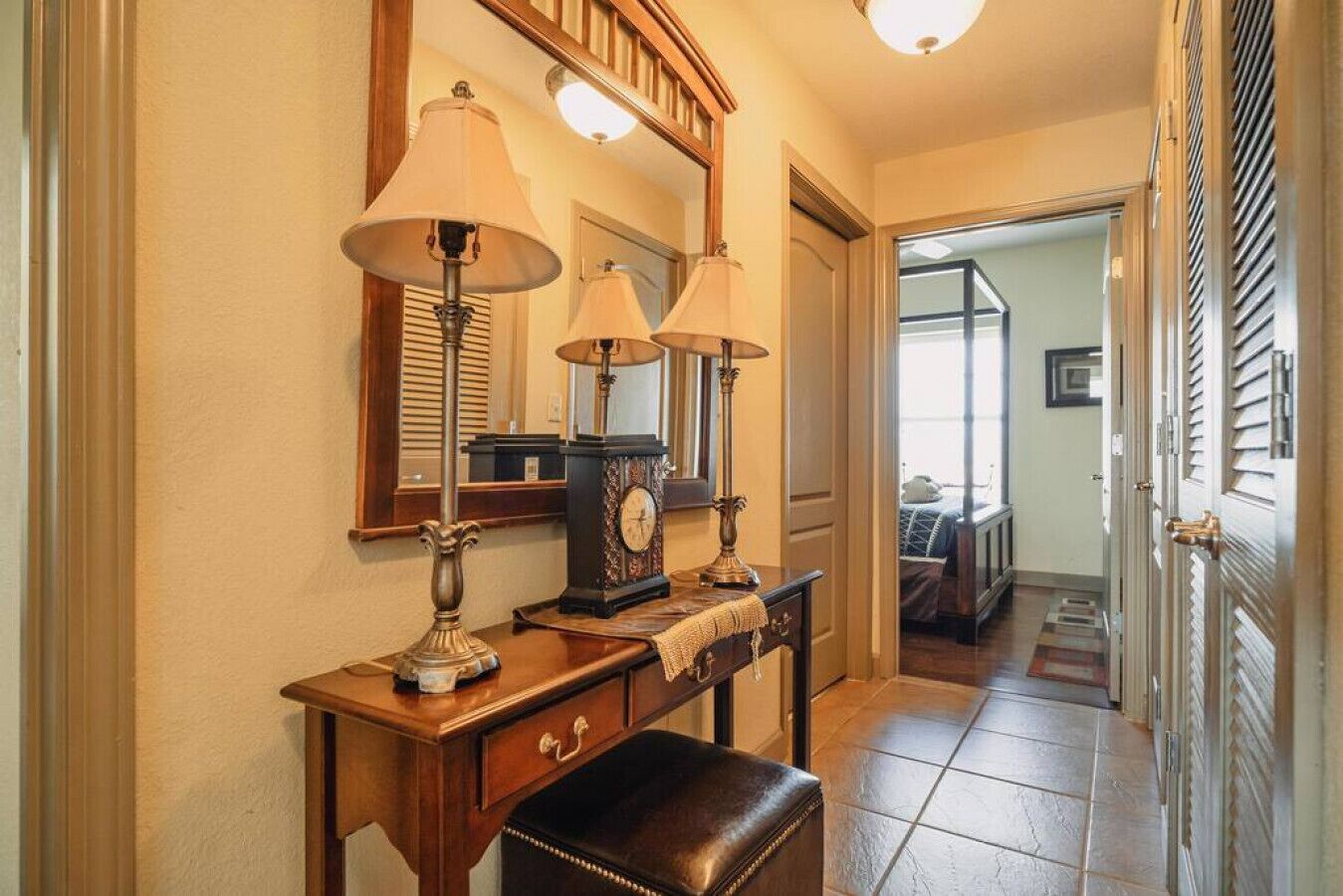 A hallway with a wooden bench, two wall-mounted lamps, a mirror, and a clock.