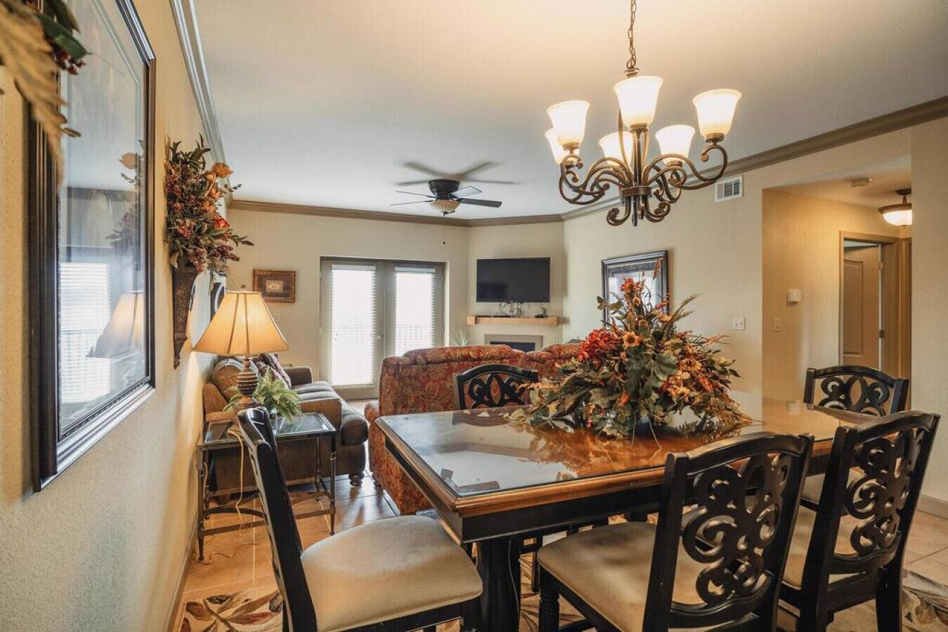 A dining area with a chandelier, a ceiling fan, and a floral centerpiece on the table.