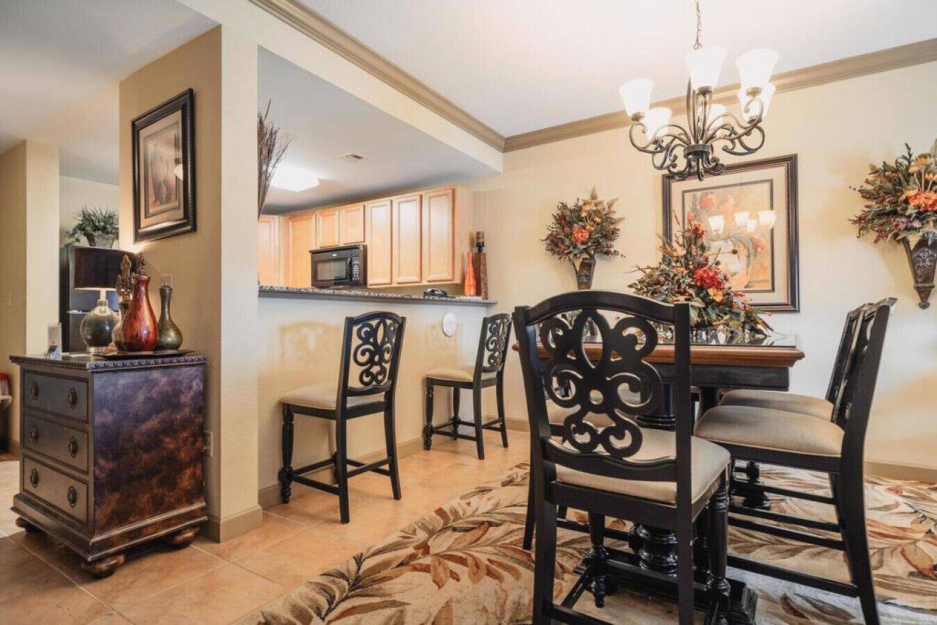 A dining area with a chandelier, wooden chairs, a table, and a kitchen in the background.