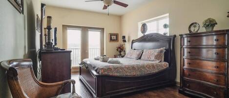 A bedroom with a large bed, a dresser, a chair, a ceiling fan, and a window with blinds.