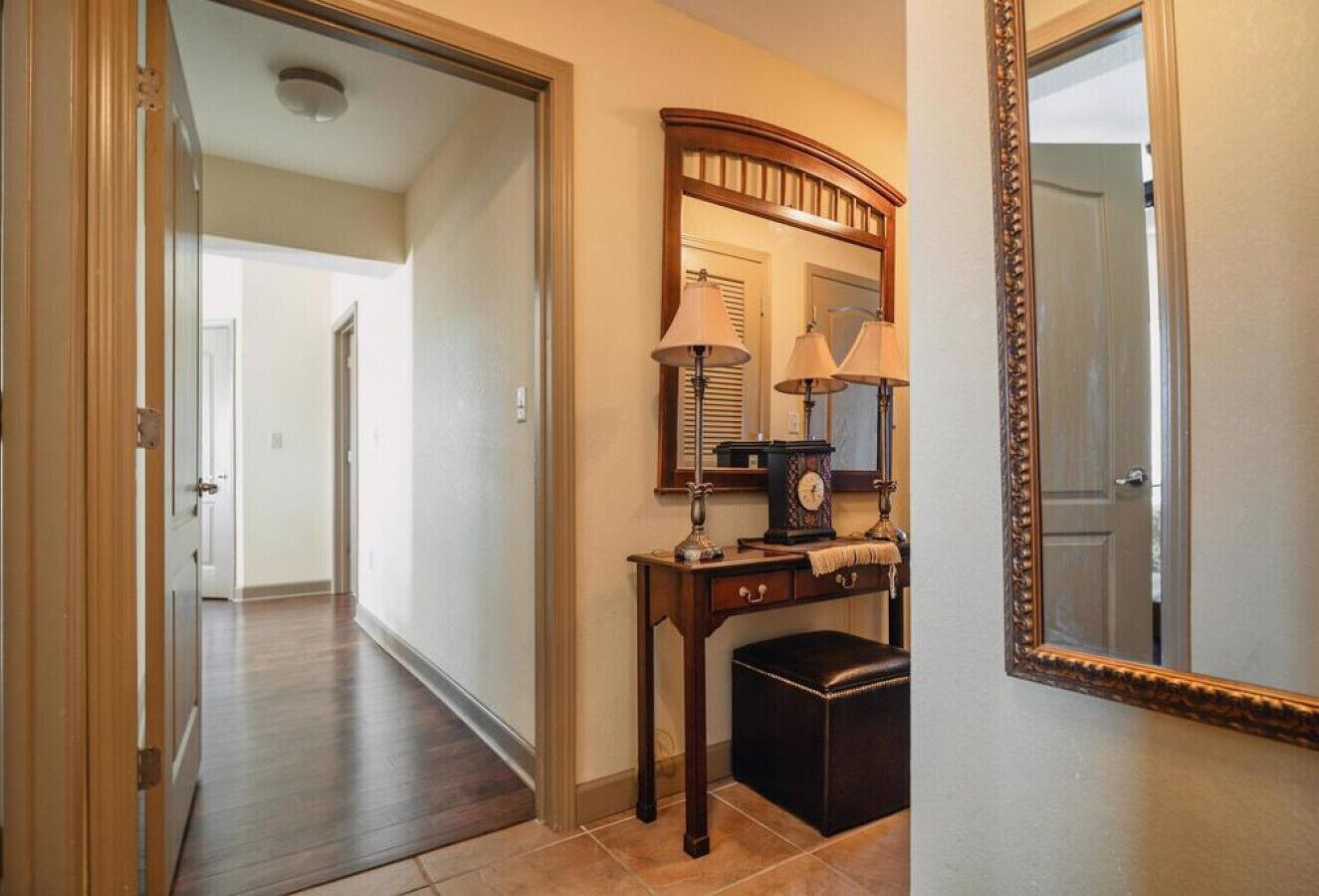 Un couloir avec un plancher en bois, un bureau avec une lampe, une horloge et un miroir.