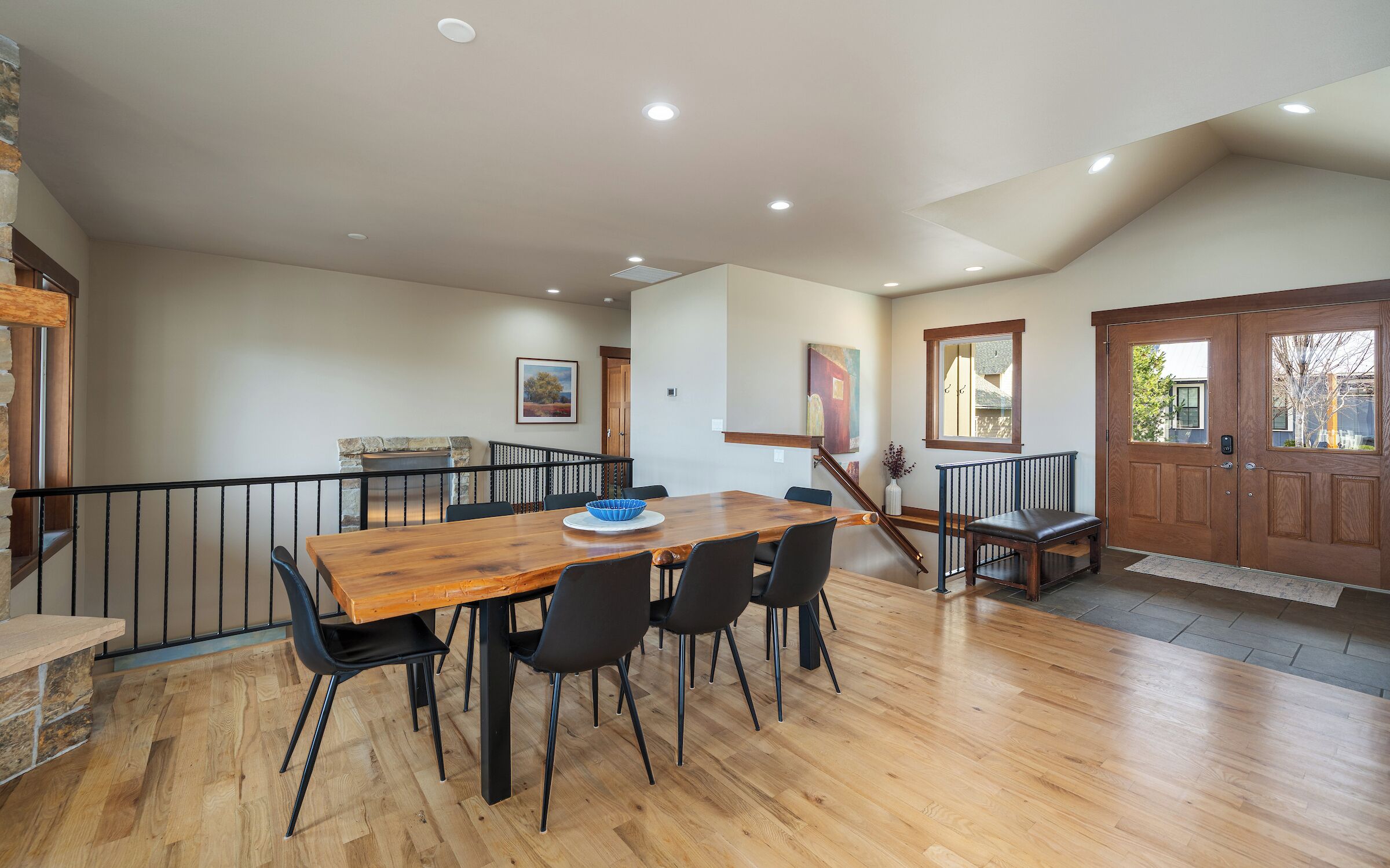 A dining area with a wooden table and chairs, a stone fireplace, and a staircase.