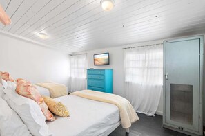 A bedroom with a bed, a blue dresser, a television on the wall, and a door with a mesh screen.
