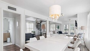 A spacious dining area with a long white table, white chairs, and a chandelier. - GULF VIEWS! 4 Bikes-Across the street from beach ! (Santa Rosa Beach)