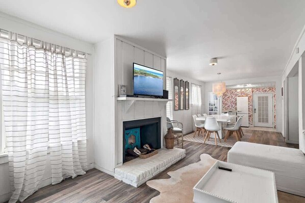 A modern living room with a fireplace, a flat-screen TV, and a dining area with a white table and chairs.