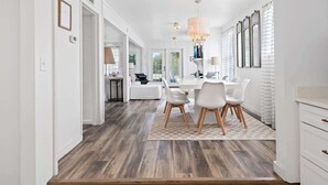 A modern kitchen with white cabinetry, a dining area with a table and chairs, and a chandelier. - GULF VIEWS! 4 Bikes-Across the street from beach ! (Santa Rosa Beach)