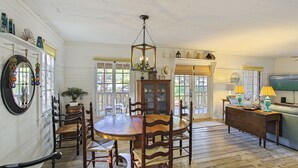 Een eetruimte met een houten tafel en stoelen, een hanglamp en uitzicht op het omliggende landschap door grote ramen.