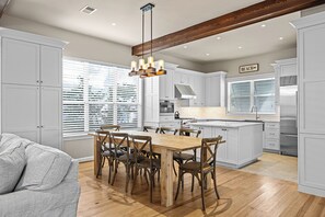A modern kitchen with white cabinetry, a wooden dining table, and a central island.