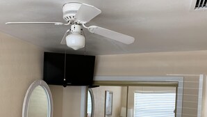 Ein Schlafzimmer mit einem Bett, einem Schminktisch, einem Spiegel, einem Fernseher und einem Deckenventilator.