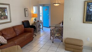 Ein Wohnzimmer mit einem braunen Ledersofa, einem Glastisch und einem Essbereich mit einer blauen Tür.