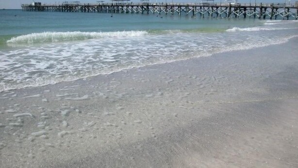 Ein Strand mit einem hölzernen Steg, der ins Wasser hineinreicht.