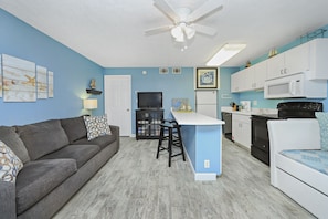 A compact living space with a kitchenette, a gray sofa, a small dining area, and a ceiling fan.