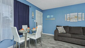 A dining area with a glass table set for four, white chairs, and a blue curtain. - QUAINT 1 BDRM!! RECENTLY UPDATED! STEPS ACROSS THE PARKING LOT TO BEACH!! (Fort Walton Beach)