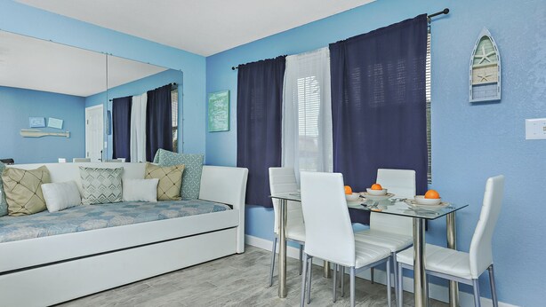 A dining area with a glass table, white chairs, and a blue wall. - QUAINT 1 BDRM!! RECENTLY UPDATED! STEPS ACROSS THE PARKING LOT TO BEACH!! (Fort Walton Beach)