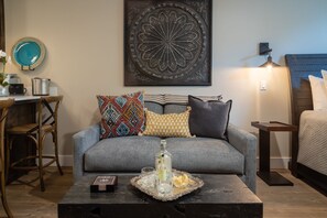 Un salon avec un canapé gris, des coussins colorés, une table basse avec un plateau, une œuvre d’art encadrée au-dessus du canapé et une lampe sur la droite.