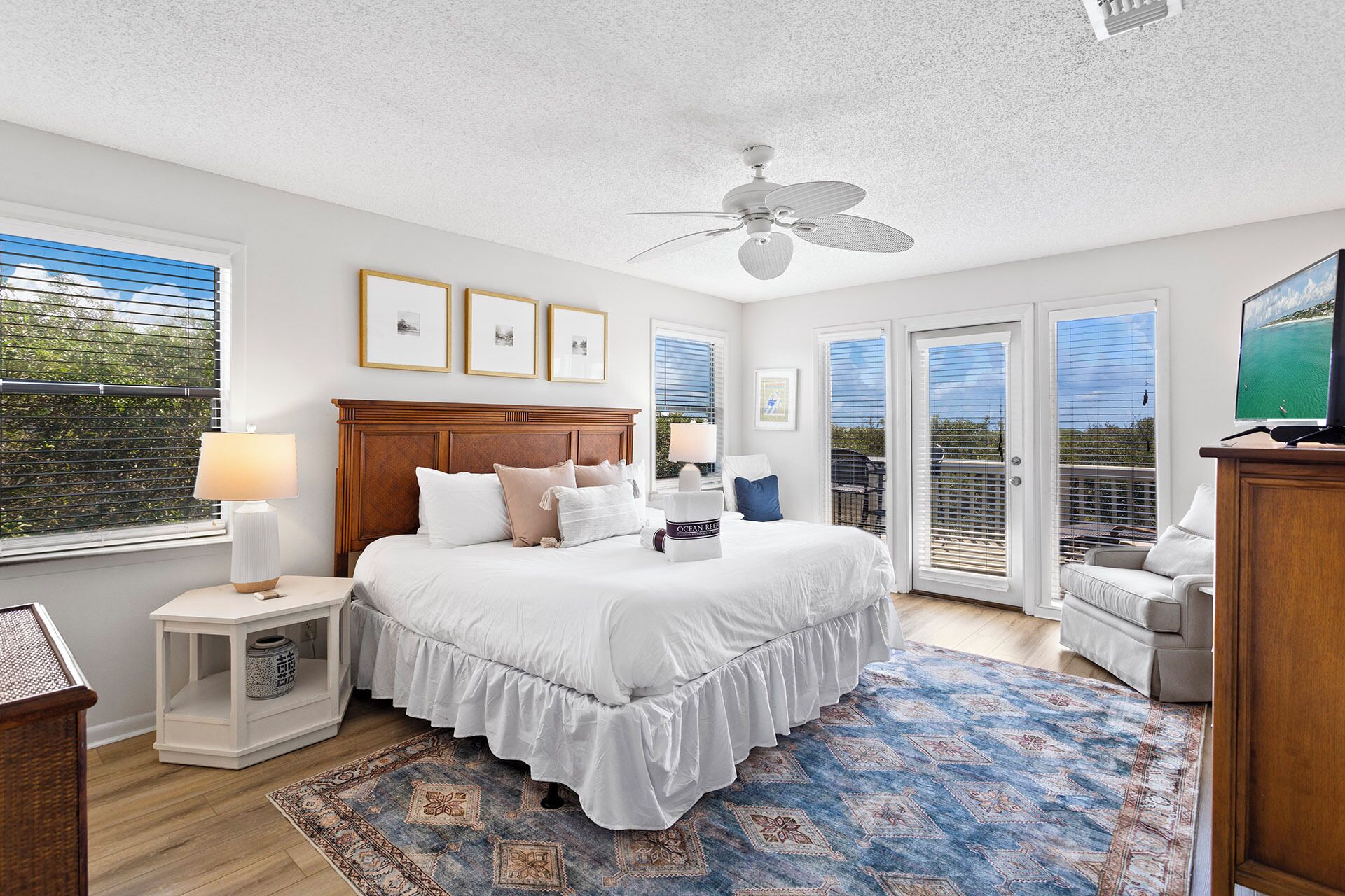 A bedroom with a large bed, a ceiling fan, and a view of the outdoors through the windows.