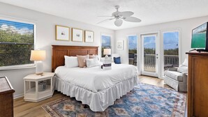 Ein Schlafzimmer mit einem großen Bett, einem Deckenventilator und Blick ins Freie durch die Fenster.