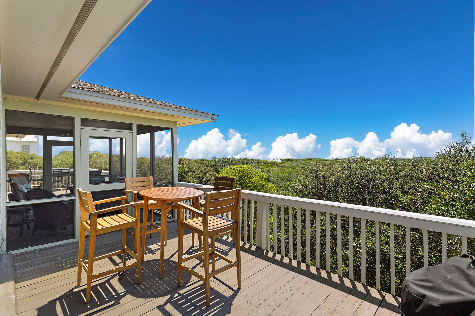 A wooden deck with a table and chairs, overlooking a lush green landscape and a clear blue sky.