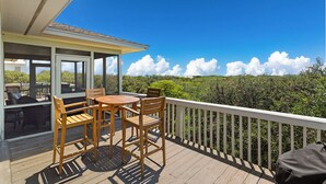 Eine Holzterrasse mit Tisch und Stühlen, die auf eine üppige grüne Landschaft und einen strahlend blauen Himmel blickt.
