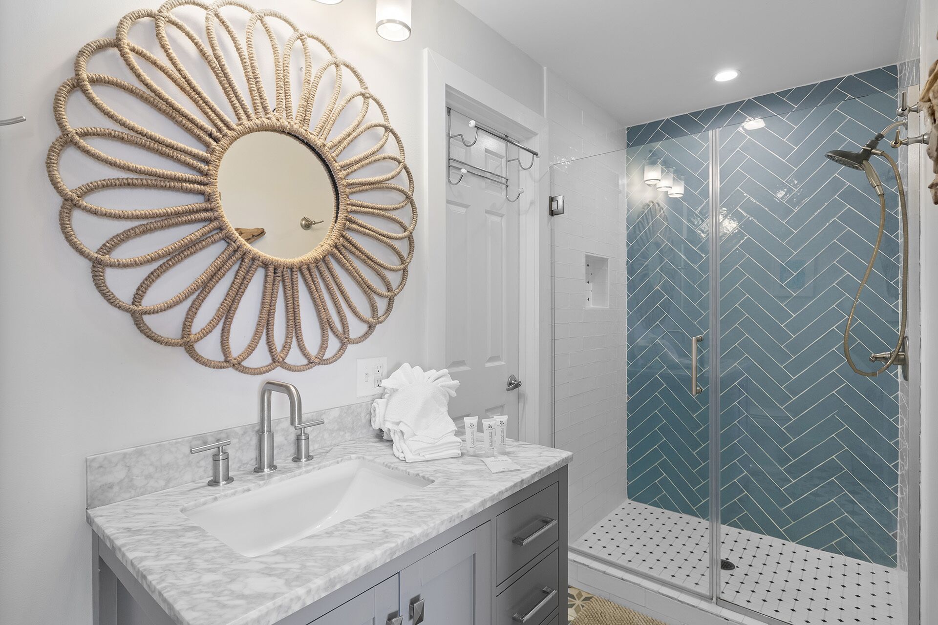 A bathroom with a marble sink, a large mirror, and a shower with a herringbone tile pattern.