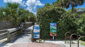 A wooden boardwalk leading to a beach area with palm trees and a signboard. - Grayton Beach Villas 103 - Gulf View, Grayton Beach, 30A, Steps to the Sand! (Grayton Beach)