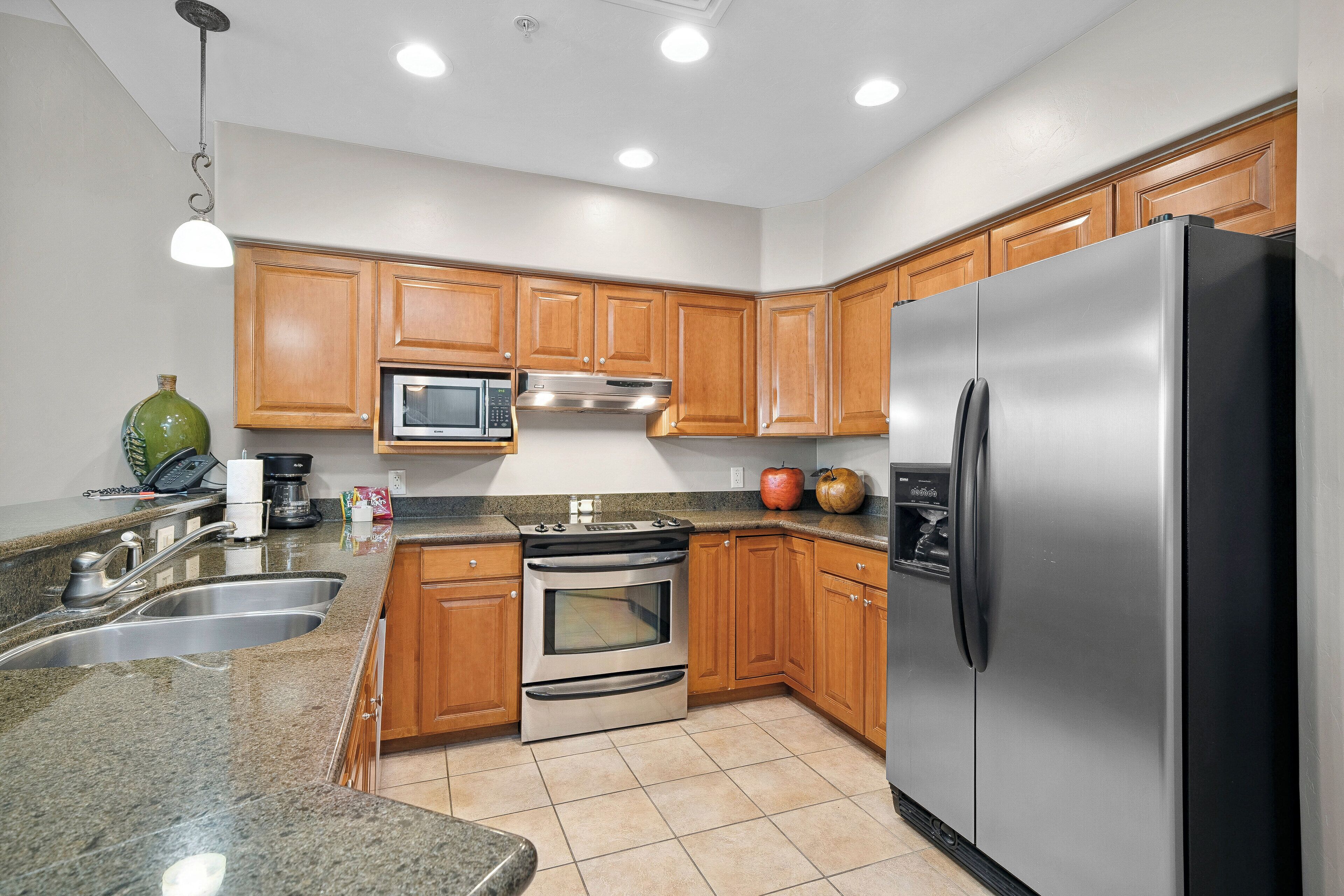 A kitchen with wooden cabinets, stainless steel appliances, granite countertops, and a tiled floor.