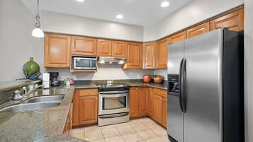 A kitchen with wooden cabinets, stainless steel appliances, granite countertops, and a tiled floor.