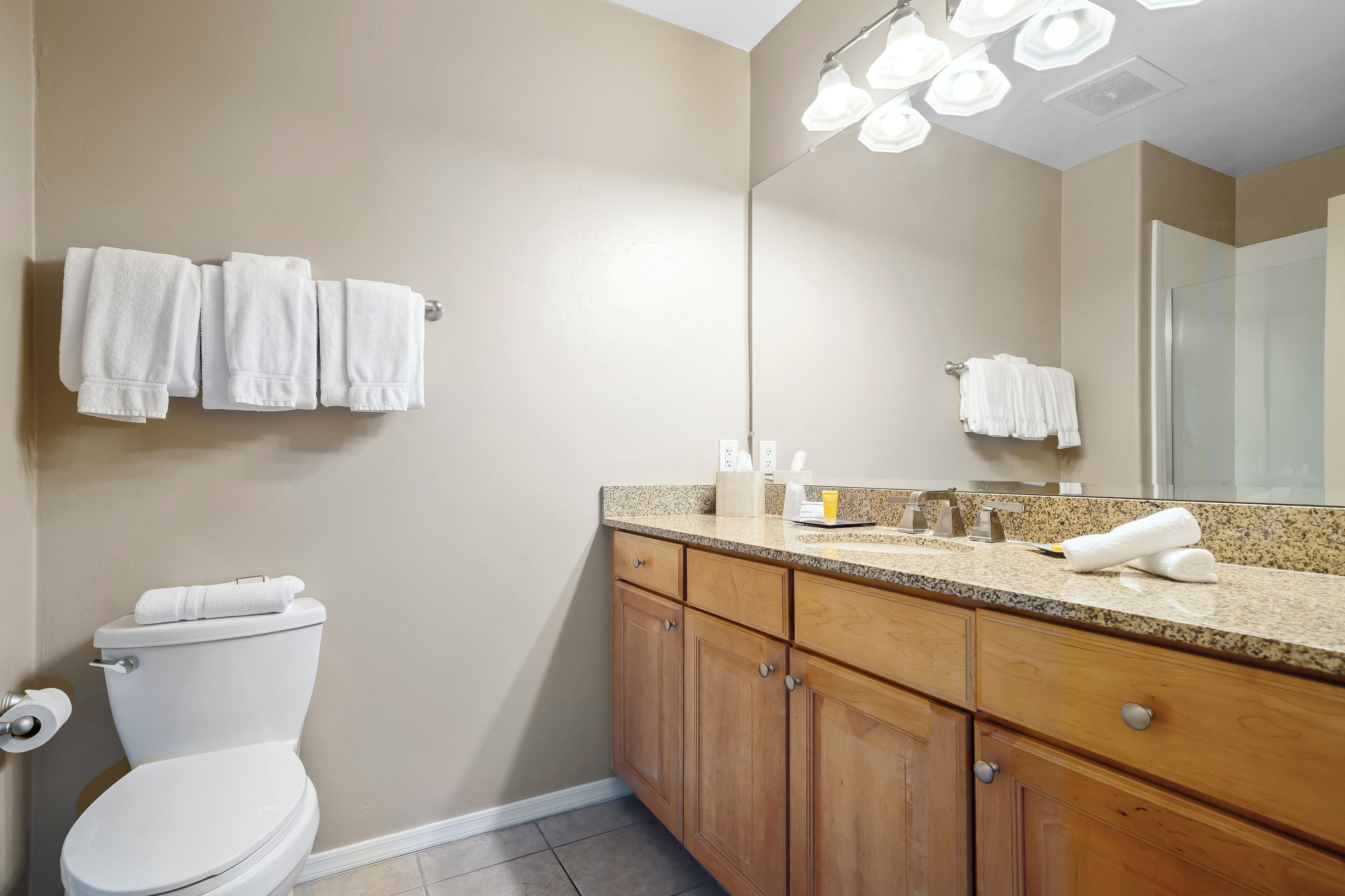A bathroom with a toilet, sink, and mirror. There are towels hanging on the wall and a towel on the counter.