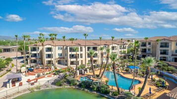 A resort with multiple-story buildings, a swimming pool, and palm trees.
