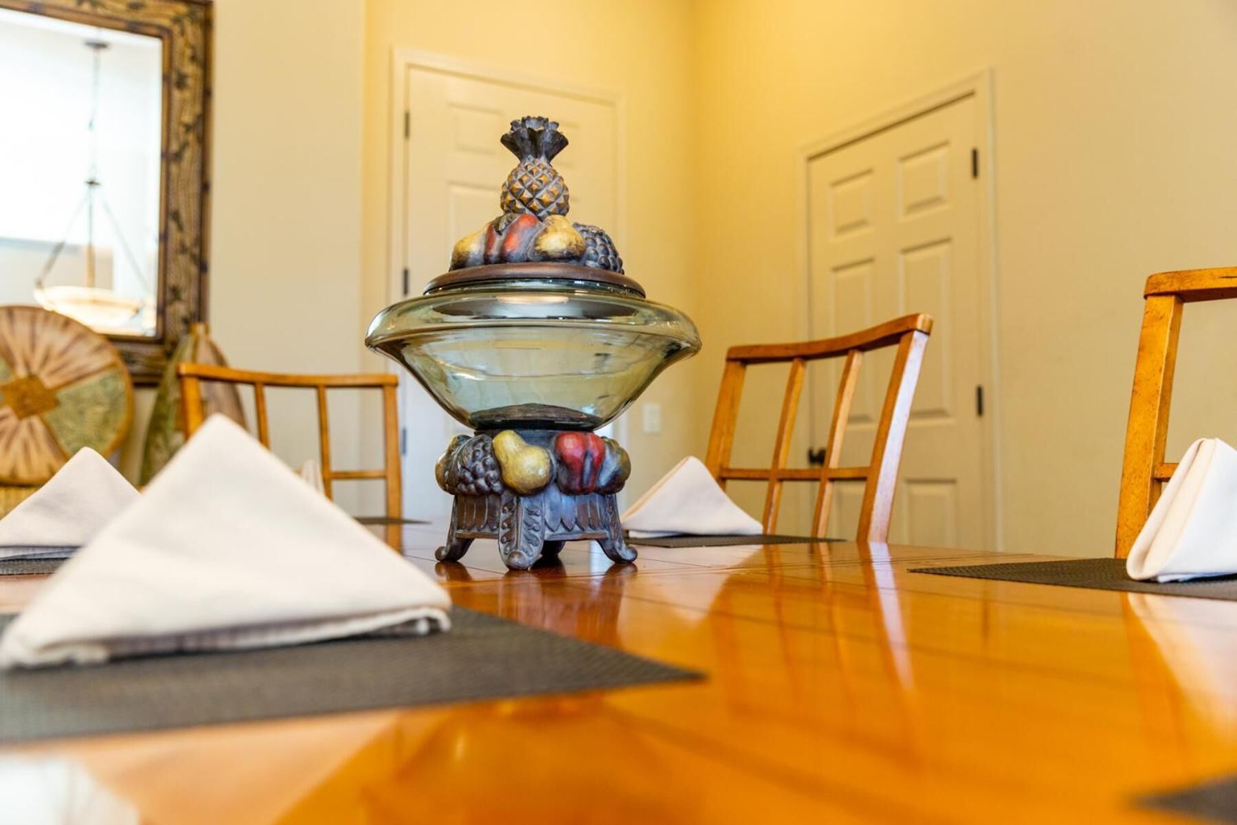 A dining table with a glass bowl centerpiece, surrounded by wooden chairs and white napkins.