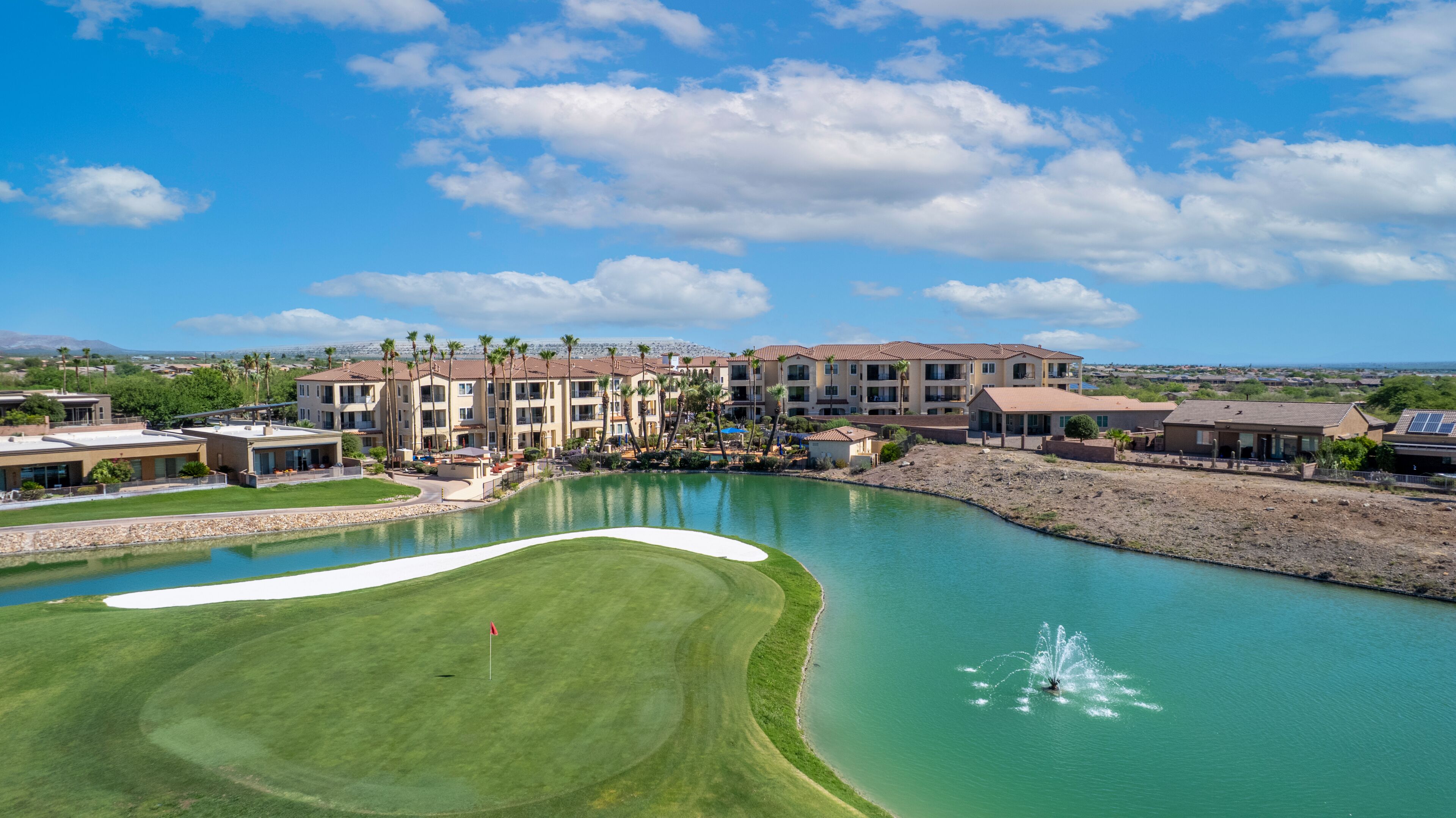 Un campo de golf con un obstáculo acuático, un putting green y un club house.
