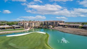 Un campo de golf con un obstáculo acuático, un putting green y un club house.