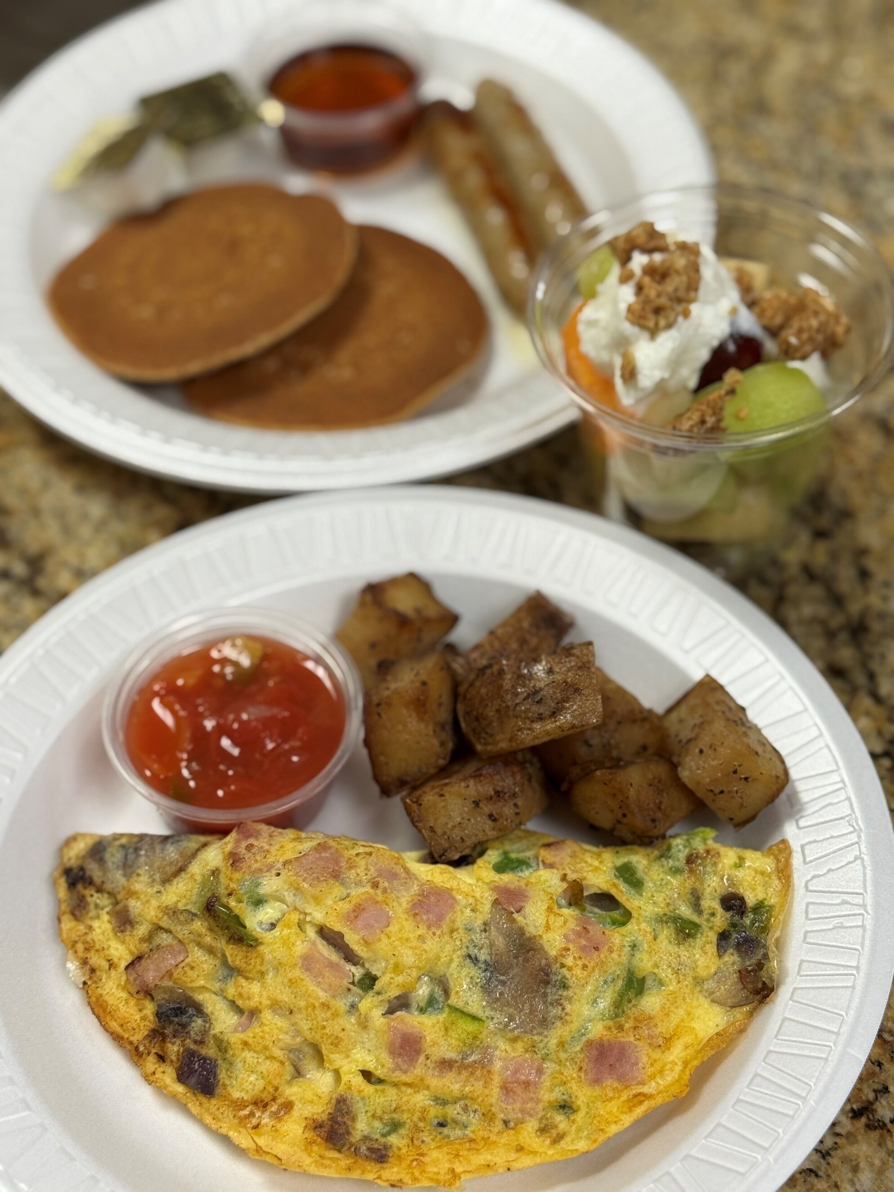 A breakfast plate with pancakes, hash browns, and a fruit salad.