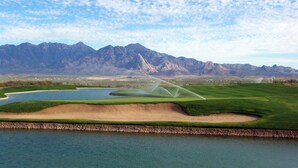 A golf course with a water hazard, sand bunkers, and a mountainous backdrop.
