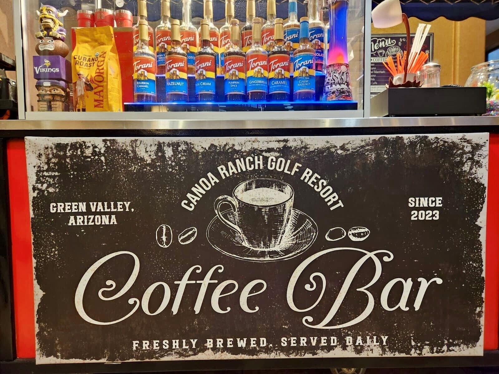 Een koffiebar met een rustiek bord waarop staat dat deze zich bevindt in Canoa Ranch Golf Resort, Green Valley, Arizona, en dagelijks verse koffie serveert sinds 2023.