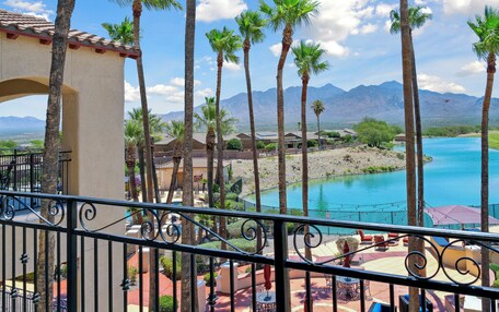 A balcony with a view of a pool, palm trees, and mountains in the background.