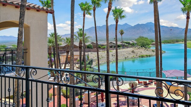 A balcony with a view of a pool, palm trees, and mountains in the background.
