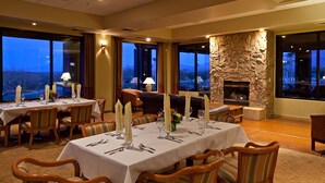 A dining area with tables set for six, a stone fireplace, and large windows offering a view of the landscape. - Canoa Ranch Golf Resort (Green Valley)
