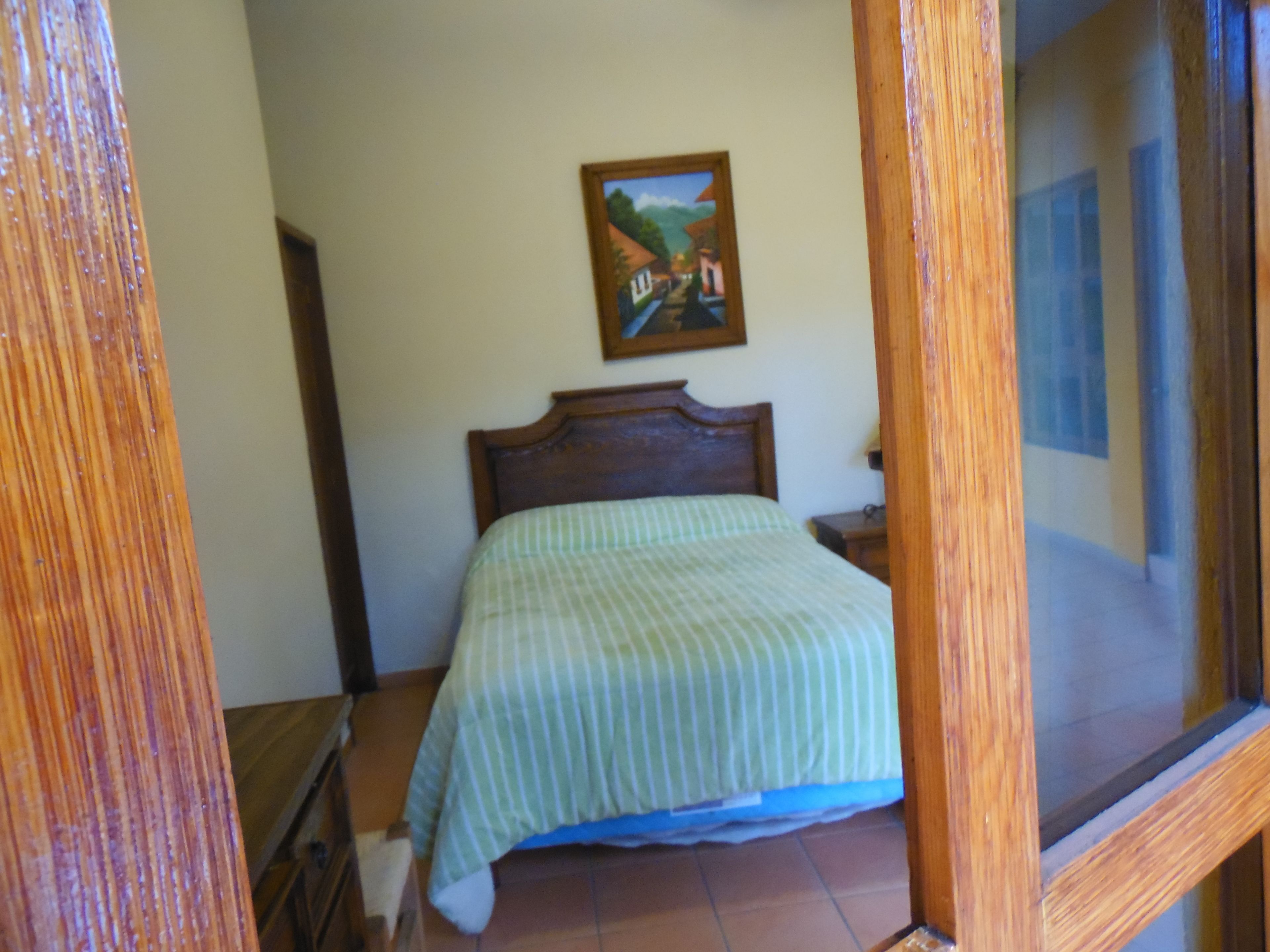Un dormitorio con cabecera de madera, cama con colcha a rayas, una mesita de noche y un cuadro en la pared.