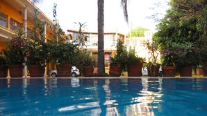 Piscina con reflejos de palmeras y edificios, rodeada de plantas en macetas y scooters estacionados.