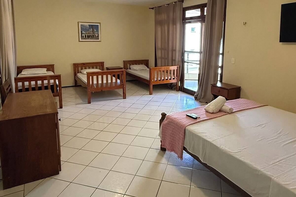 A room with a bed, two wooden chairs, a small table, and a window with curtains.