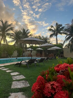 A pool area with lounge chairs and umbrellas, surrounded by palm trees and a clear sky. - Pousada Italia Beach (Aquiraz)