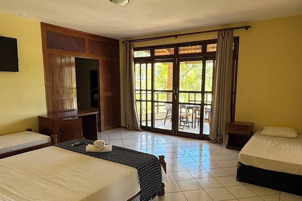 A hotel room with two beds, a TV, a wooden cabinet, and a balcony with curtains.