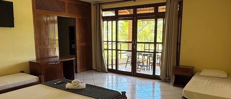A hotel room with two beds, a TV, a wooden cabinet, and a balcony with curtains.