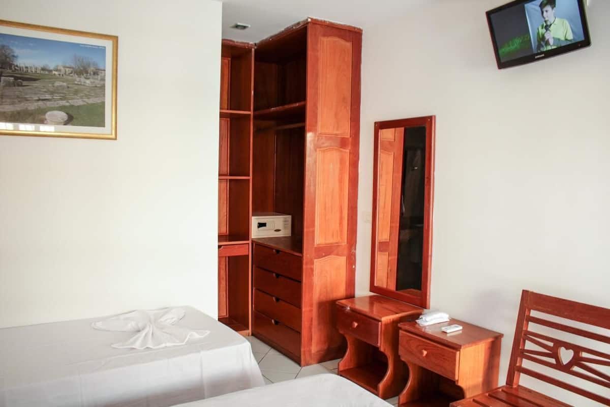 A bedroom with a bed, a wooden desk, a mirror, a wardrobe, and a television on the wall.