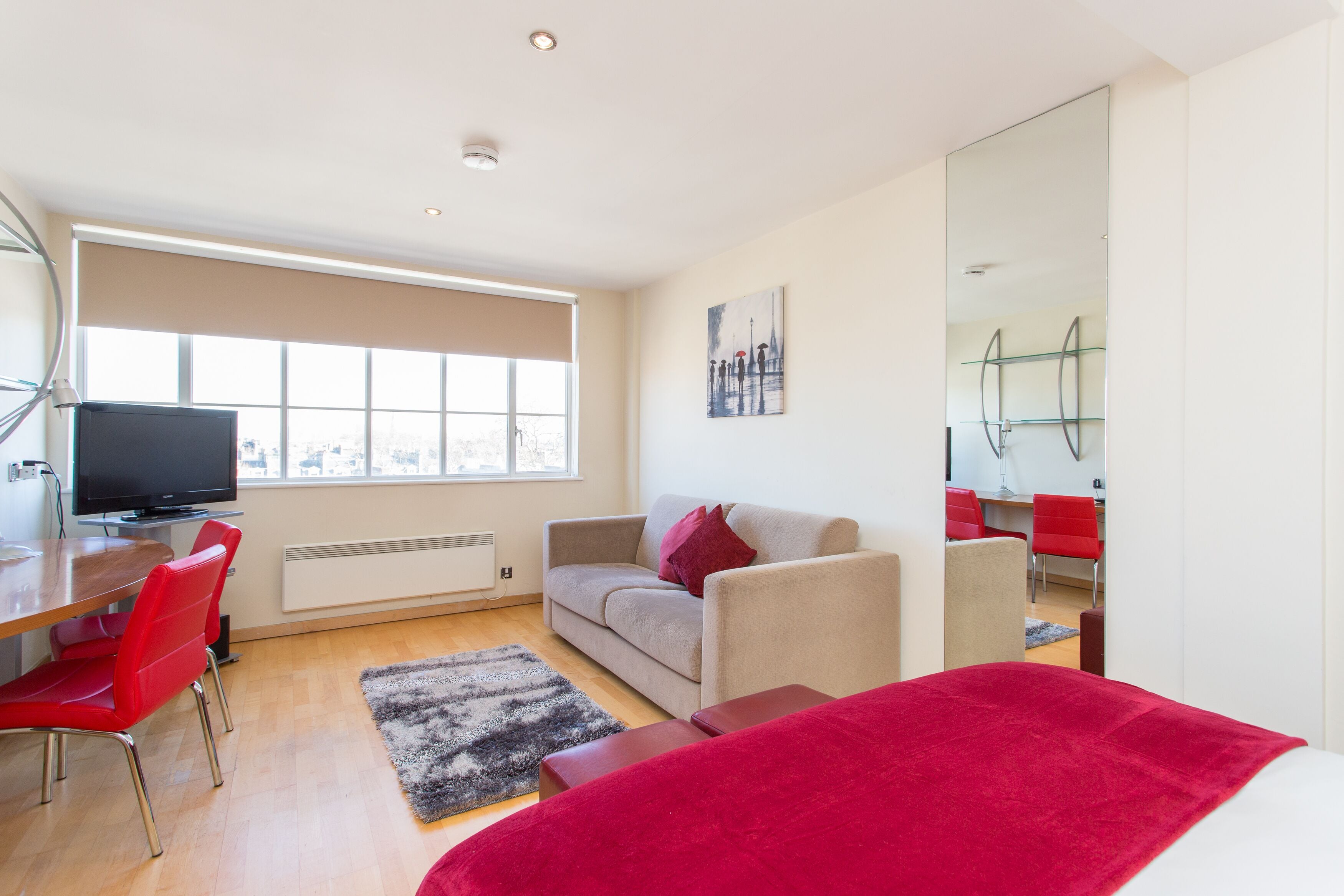 Una habitación moderna con un sofá, sillas rojas, un televisor, un ventanal grande y un espejo.