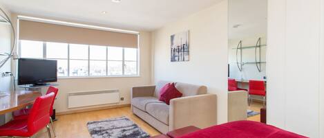 A modern room with a sofa, red chairs, a TV, a large window, and a mirror.