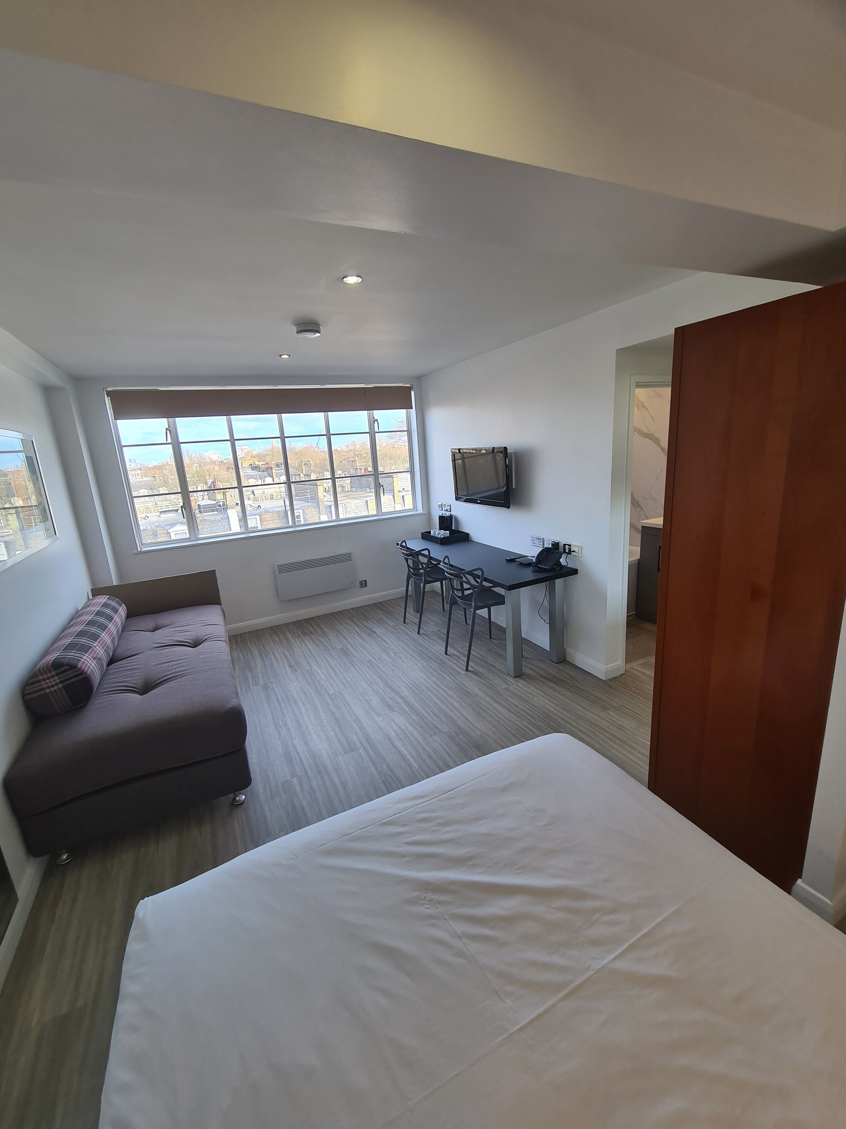Une chambre moderne avec un grand lit, un canapé, un bureau avec une chaise, une télévision et une fenêtre donnant sur la ville.