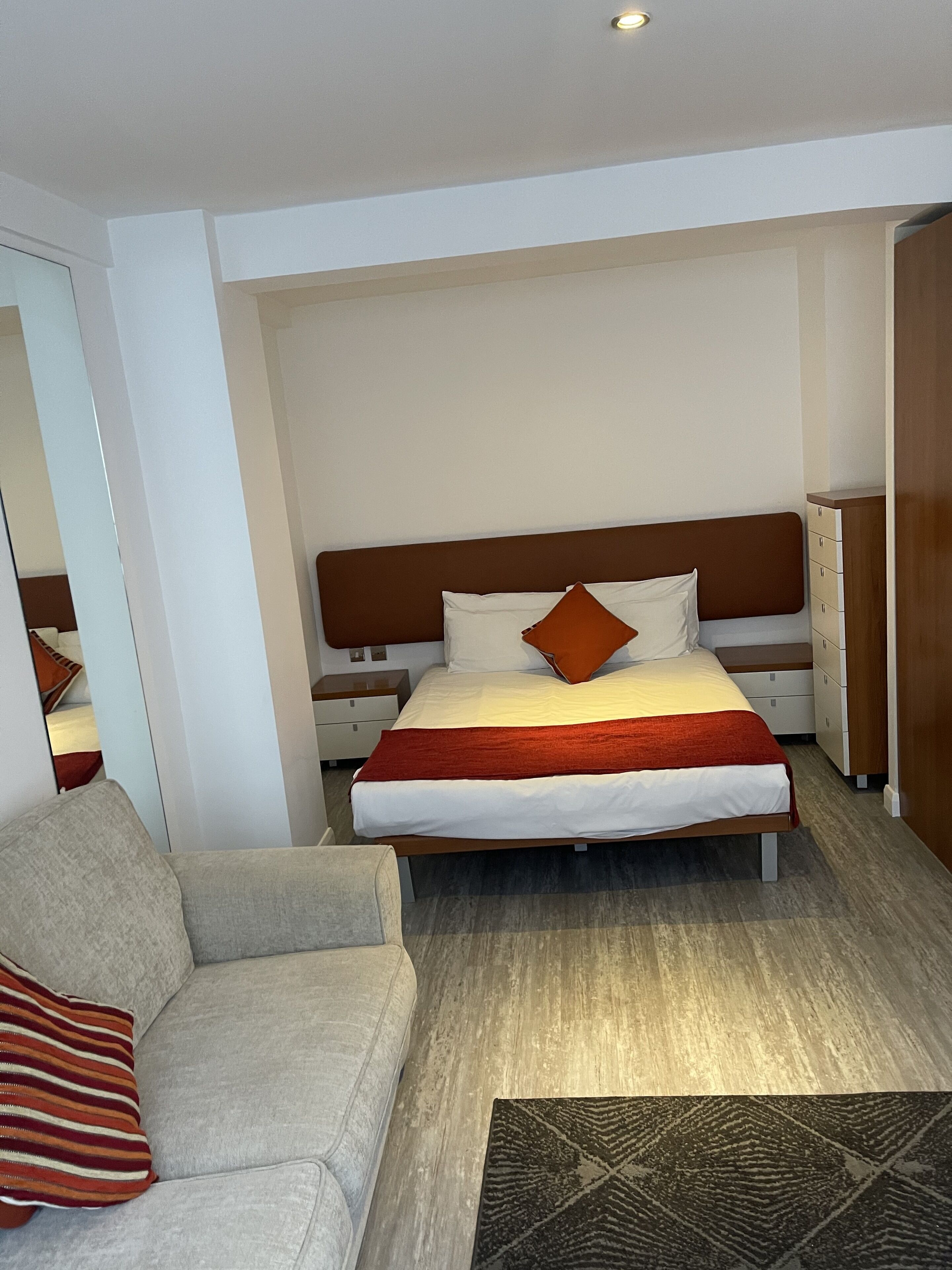 A modern hotel room with a large bed, a sofa, a nightstand, and a wardrobe.